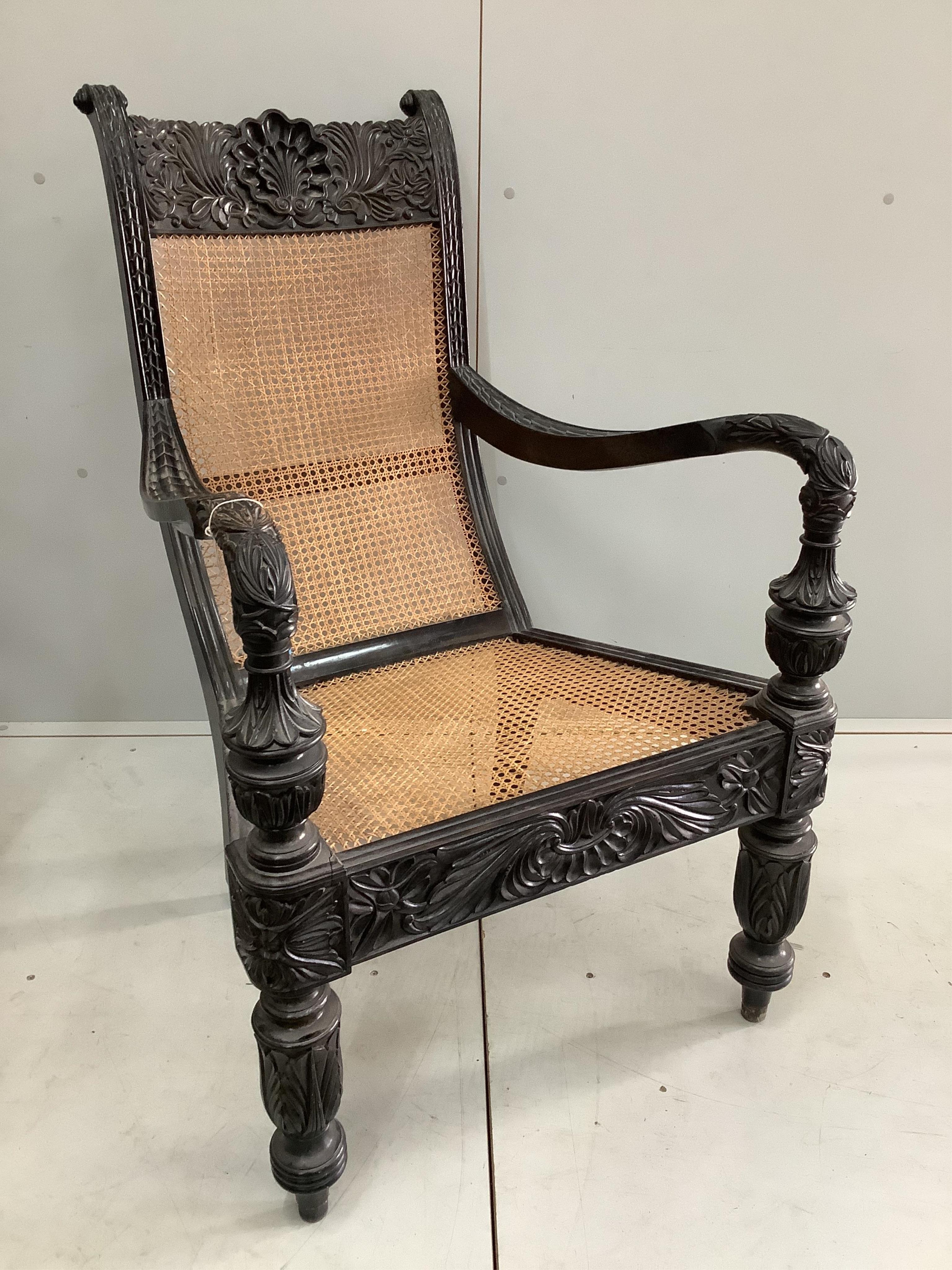 A 19th century Anglo-Indian carved ebony library armchair, with a caned seat and back, width 60cm, depth 76cm, height 102cm. Condition - good